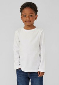 Witte lange mouwen t-shirt van zachte katoen, met een ronde halslijn en een relaxte pasvorm, gecombineerd met blauwe denim jeans. Eenvoudig ontwerp, zonder patronen.