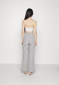 Top cropped de cetim branco com alças ajustáveis, apresentando um fechamento de botão nas costas. Combinado com calças de perna larga cinza claro de cintura alta.