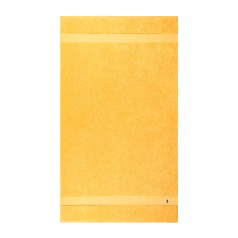 Κίτρινη βαμβακερή πετσέτα με υφασμένη επιφάνεια, δύο οριζόντιες λωρίδες και ένα μικρό μπλε λογότυπο στην κάτω γωνία. Ορθογώνιο σχήμα.