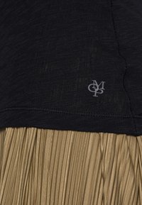 Czarna, fakturowana bluzka z widocznym logo oraz złota spódnica w plisę. Spódnica ma błyszczące wykończenie z równomiernie rozmieszczonymi plisami.