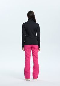 Zwart langslavend shirt met een hoge hals, gecombineerd met felroze broek met ritsen bij de enkels, beide in een getailleerde stijl.