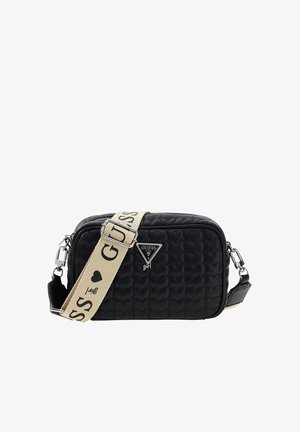 Bolso bandolera negro acolchado con logo "Guess", correa de hombro beige ajustable con texto negro y diseños de corazones, herrajes plateados.
