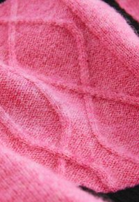 Tissu tricoté doux rose pâle avec un motif en losange texturé et des fibres duveteuses visibles, créant une apparence chaleureuse et confortable.