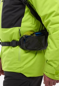 Veste imperméable vert fluo avec des accents noirs, accompagnée d'une ceinture noire dotée de zippers et d'objets bleus visibles à l'intérieur.