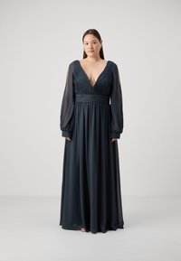 Robe longue bleu marine en tissu fluide, dotée d'un décolleté en V profond, d'un corsage plissé et de manches longues transparentes.