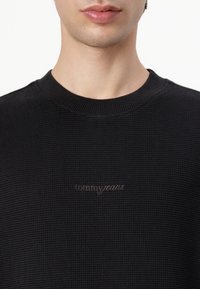 Sort waffle-strik sweater med ribbet rund halsudskæring. Har et diskret "tommy jeans" logo i mørk tråd på forsiden.