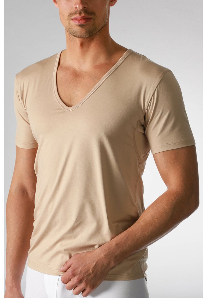 Beżowy t-shirt z krótkim rękawem i głębokim dekoltem w serek, wykonany z gładkiego materiału, o dopasowanym kroju z delikatnymi detalami przeszyć wzdłuż szwów.