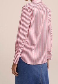 Red and white striped shirt with long sleeves, button cuffs, a rounded hem, and a collared neck, made from a lightweight fabric.