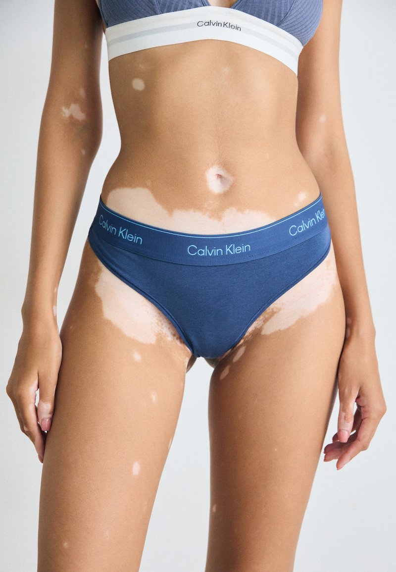 Caleçon en coton bleu marine avec une large ceinture comportant le logo "Calvin Klein". Texture lisse et design ajusté, mettant en valeur les variations de ton de peau.