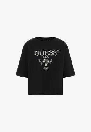 Crop top noir à manches courtes avec du texte en sequins argentés "GUESS U.S.A." et un point d'interrogation, avec "Washed Jeans" imprimé autour.
