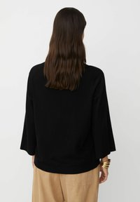 Maglione nero a maniche a campana 3/4, con texture liscia, orlo a costine e design semplice, abbinato a pantaloni beige chiaro.