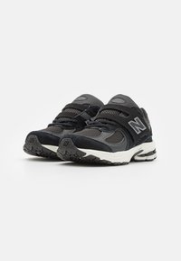 Des chaussures de sport noires avec des matériaux en maille et en daim, des fermetures à lacets et à sangle, une semelle texturée et des accents réfléchissants.
