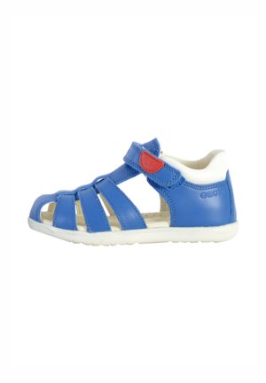 Sandale en cuir bleu avec semelle blanche, design ouvert, sangle à boucle auto-agrippante, accent rouge sur la sangle et trous de ventilation pour la respirabilité.