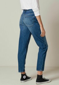 Jeans de mezclilla azul de cintura alta con un corte relajado, piernas ajustadas y dos bolsillos traseros, combinados con zapatillas negras de caña alta.