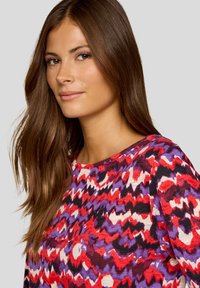 Purple, red, and white patterned top featuring a round neckline and short sleeves, made of a lightweight, textured fabric.