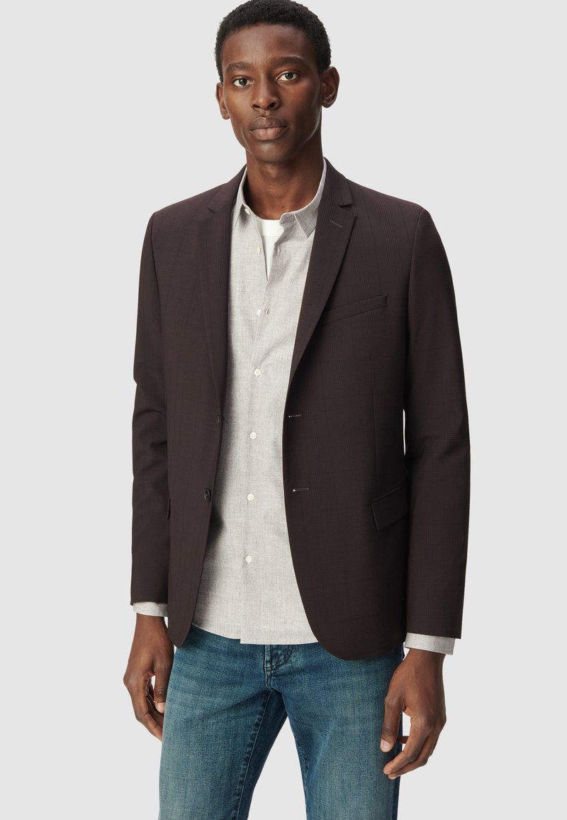 Ciemnobrązowa marynarka z fakturowanym wykończeniem, na pojedynczy guzik, slim fit. Noszona na jasnoszarym guzikowym swetrze i niebieskich dżinsach.