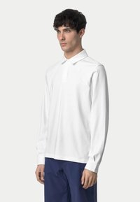 Polo shirt bianco a maniche lunghe in cotone con colletto classico, caratterizzato da un logo discreto sul petto e orlo dritto.