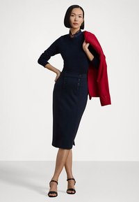 Mørkeblå ullblanding genser og blyantskjørt med knappdetaljer, paret med en rød blazer og svarte hæl sandaler.