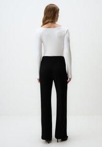 Un haut blanc à manches longues côtelé associé à un pantalon large noir taille haute, avec une finition lisse et un léger éclat, porté avec des talons.