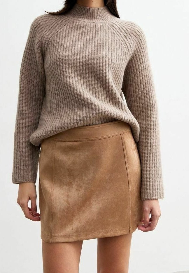 Femme portant un pull côtelé beige rentré dans une mini-jupe en daim couleur sable, debout devant un fond blanc uni.