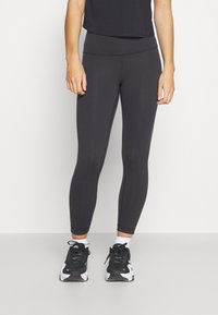 Schwarze, enganliegende Leggings mit hohem Bund aus dehnbarem Material. Kombiniert mit schwarzen und weißen Sportschuhen und Knöchelsocken.