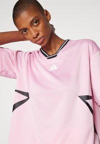Jersey atlético de color rosa claro con mangas cortas, acentos negros, logo blanco y diseño de cuello en V, fabricado con un tejido suave y transpirable.