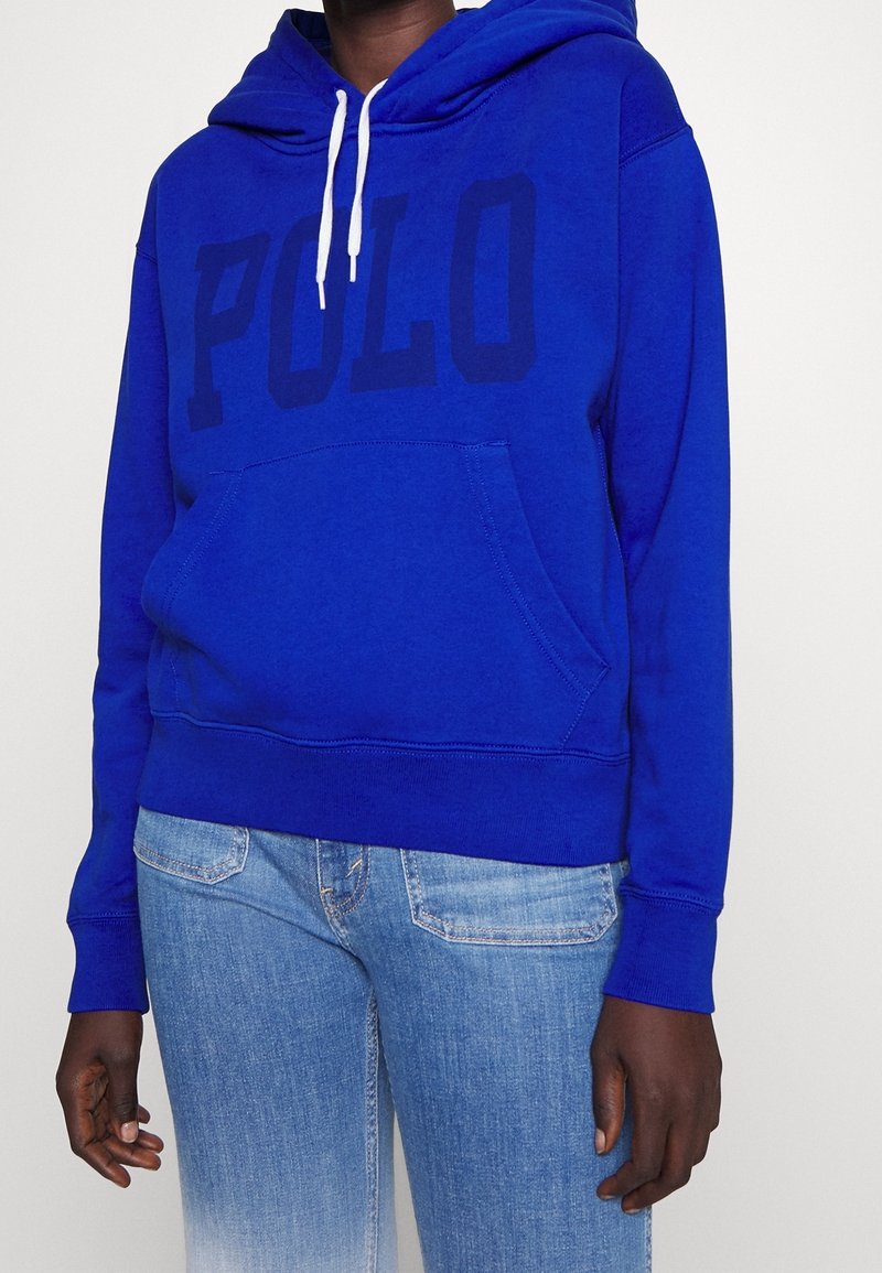 Sweat à capuche bleu en mélange de coton, avec une poche avant, des cordons blancs et un grand logo "POLO" noir imprimé sur la poitrine.