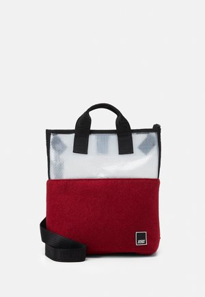 Sac cabas rouge et transparent avec des poignées et une sangle noires, arborant un logo Jost noir et blanc en bas à droite.