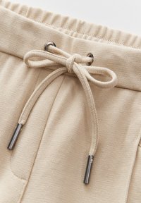 Beige sweatpants hebben een textuurstof, een elastische tailleband en een verstelbaar koord met zilveren hardware accenten.