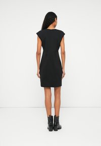 Melna bezjaka kleita ar strukturētām plecu daļām, pieguļošs siluets un aizmugurējais rāvējslēdzējs. Valkāta ar potīšu zābakiem, gluda tekstūra, minimālisma dizains.