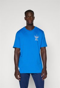 Blue cotton t-shirt with short sleeves, featuring an embossed white logo on the chest area, relaxed fit, solid color, and smooth texture.