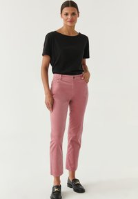 Roze corduroy broek met een slim fit, voorzakken en een metalen knoop, gecombineerd met een zwart t-shirt met korte mouwen en zwarte instappers.