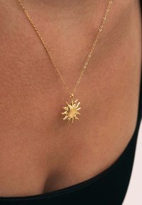 Collier en or avec un pendentif en forme de soleil aux rayons pointus, surface texturée et chaîne délicate. Porté contre la peau.