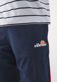 Marina atletiska shorts med röda sidodetaljer, tillverkade av mjukt material. Har en vit "ellesse"-logotyp på vänster ben.