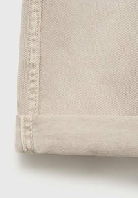 Beiger Denim-Stoffabschnitt mit umgeschlagenem Saum, der eine diagonale Webstruktur, sichtbare Nähte und eine glatte Oberfläche aufweist.