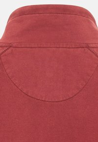 Chemise rouge à col avec une texture lisse, des détails de couture subtils et un empiècement arrière incurvé.