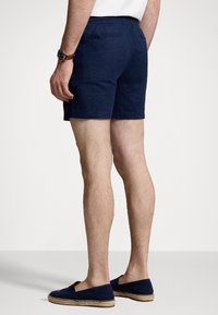 Navy blue linen shorts with an elastic waistband, featuring a back pocket and subtle branding. Worn with navy espadrilles.