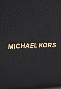 Czarna teksturowana powierzchnia z nazwą marki "MICHAEL KORS" w złotych literach wielkich.