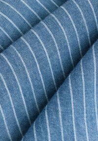 Blue fabric with white pinstripes, showing a textured weave. The fabric is folded, highlighting the pattern and depth of the material.