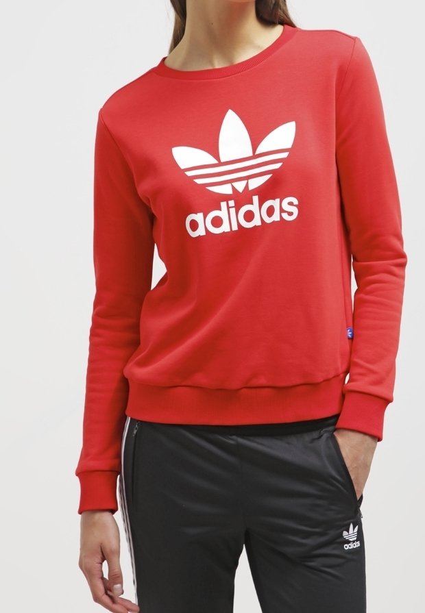 Röd sweatshirt med en vit Adidas-logotyp, rund halsringning och ribbade ärmslut. Matchad med svarta byxor med vita accenter och sidosträck.