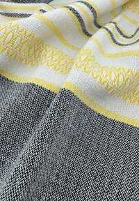 Textielstof met een mix van zwarte, witte en gele strepen, voorzien van een gestructureerd oppervlak en complexe patronen langs de randen.