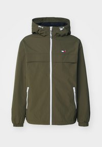 Olivgrön jacka med huva, vit dragkedja och två fickor med dragkedja. Har ett horisontellt bröstpanel och en logo patch i röd, vit och blå.