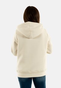 Sudadera con capucha color crema de corte relajado, con puños y dobladillo de canalé. Textura suave, costuras visibles y capucha con cordón.
