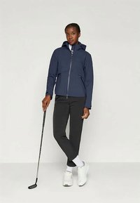 Navy waterproof jacket with a front zipper, two side pockets, and a hood; paired with black pants and white athletic shoes.