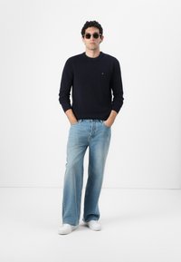 Granatowy sweter dziany, jasne, szerokie dżinsy, białe sneakersy i okrągłe okulary przeciwsłoneczne. Prosty design z kontrastującymi fakturami i kolorami.