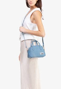 Borsa a mano in pelle blu con doppi manici superiori e una tracolla staccabile. Texture liscia, forma rotonda e dettaglio del logo sulla parte frontale.