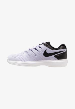 Zapatilla deportiva en tonos púrpura y negro, con material de malla, cordones planos y suela blanca. Presenta un destacado logo de Nike en negro en el lateral.