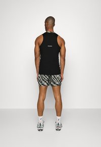 Černý bezrukávový top a vzorované šortky v odstínech zelené a šedé. Boty s reflexními detaily a bílé ponožky viditelné.