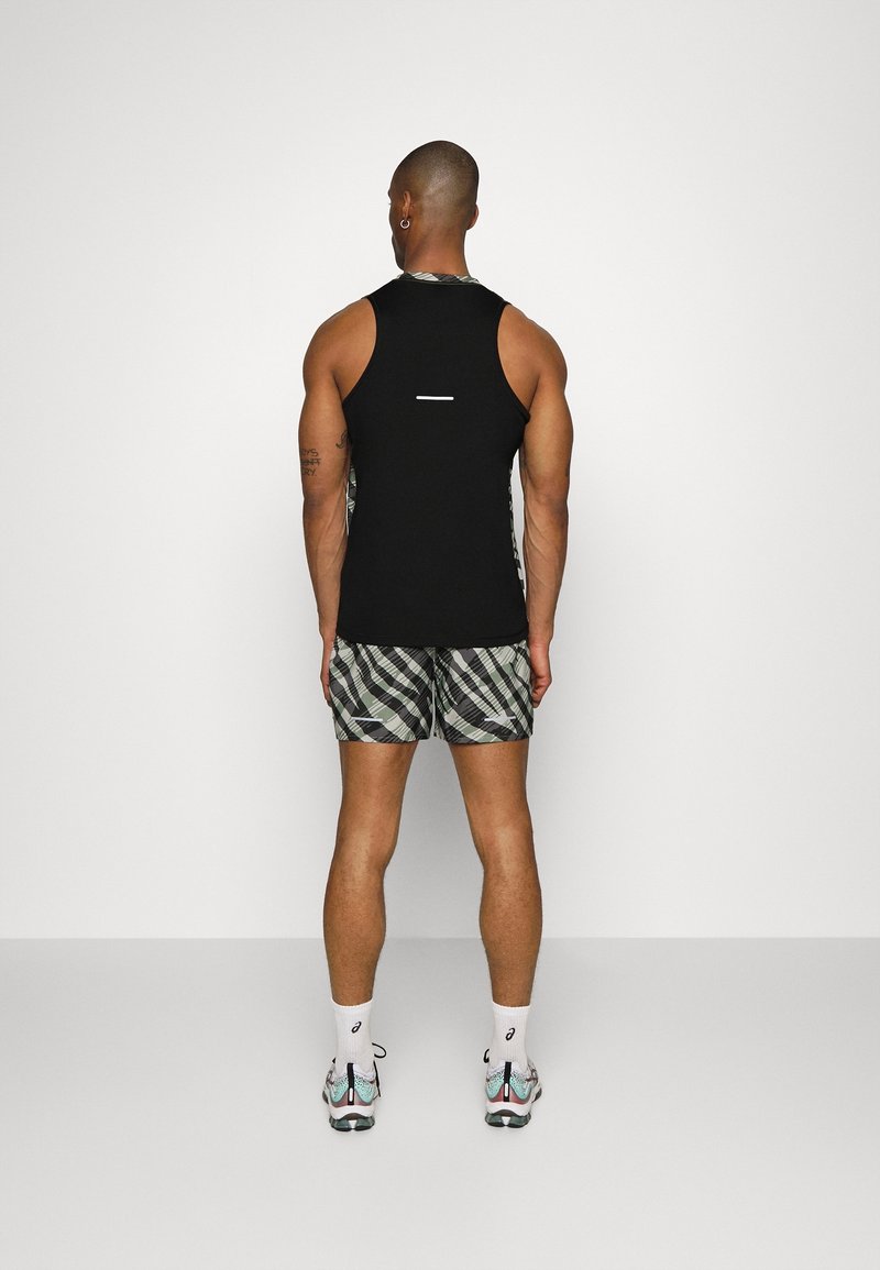 Černý bezrukávový top a vzorované šortky v odstínech zelené a šedé. Boty s reflexními detaily a bílé ponožky viditelné.