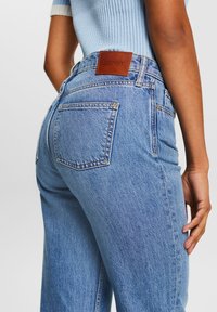 Jeans de mezclilla en azul claro, con un corte clásico, dos bolsillos traseros y una etiqueta de marca de cuero marrón en la cintura. Tejido texturizado.